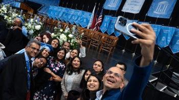 A graduate surrounded by her family, including one man who's taking a group selfie on a phone at U.N.C. Chapel Hill's Winter Commencement.